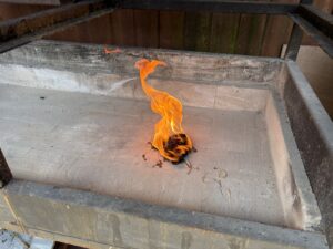 Small orange flame burning on a dusty concrete surface inside a metal fire pit.