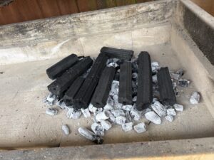 Charcoal briquettes and ash inside a rectangular concrete fire pit, ready to be lit outdoors.