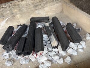 Charcoal briquettes arranged in a pit with white ash and glowing embers beneath them