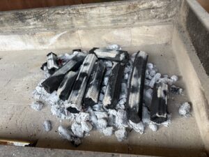 Charred wooden logs and white ash in a brick-lined fire pit.